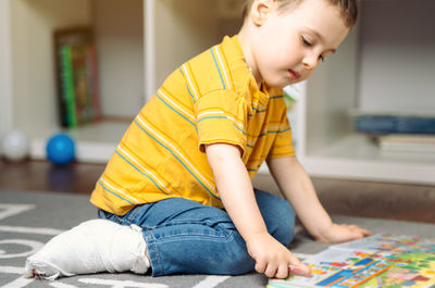Toddler boy with a bandage or cast on his leg plays with colourful book. fracture of a foot 