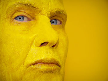 Close-up portrait of woman with face paint against yellow background