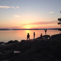 Silhouette people standing on beach against sky during sunset