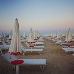 Lounge chairs with parasols at beach against clear sky during sunset