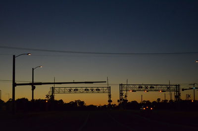 Silhouette of railroad crossing and road at sunset