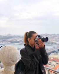 Woman photographing on camera against sky