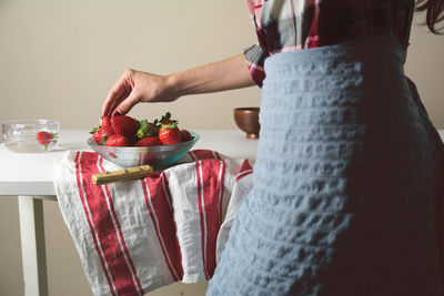 Midsection of woman taking strawberry from bowl on table