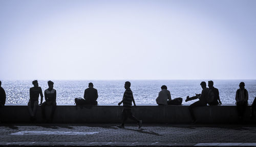 People sitting on retaining wall against sea