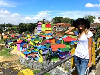 Woman wearing hat standing against colorful houses during sunny day