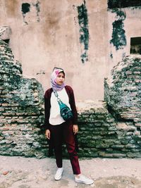 Full length portrait of young woman standing against wall