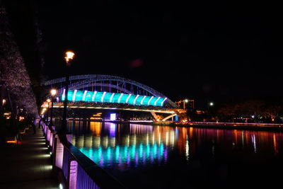 Illuminated footbridge over river against sky at night