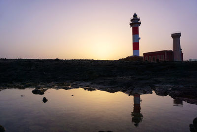 Lighthouse by lake against sky during sunset