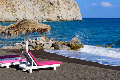 Deck chairs on rocks by sea against sky