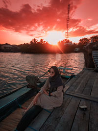 Woman sitting on boat against orange sky during sunset