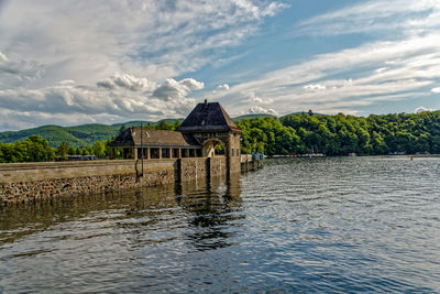 House by lake and building against sky