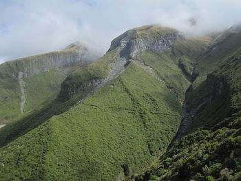 Scenic view of green mountains against cloudy sky