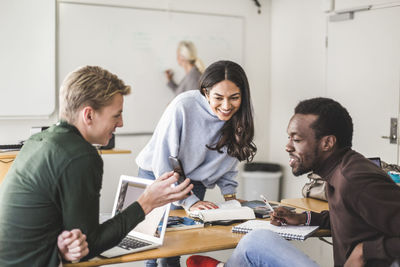 Smiling young man showing smart phone to friends in classroom