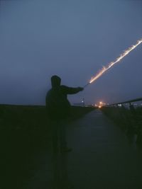 Rear view of silhouette man standing against sky at night