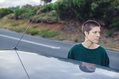 Woman looking away while standing by car on roadside