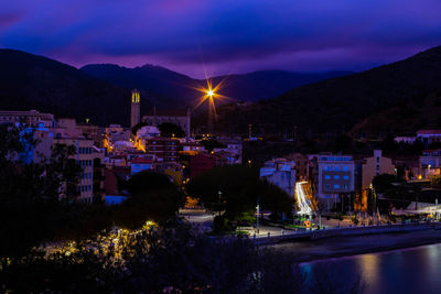 Illuminated buildings by river against sky at night