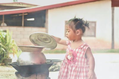 Baby girl opening utensil on wood burning stove at backyard