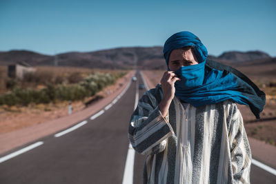 Portrait of man standing on road against blue sky