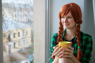 Portrait of a beautiful young woman drinking from window