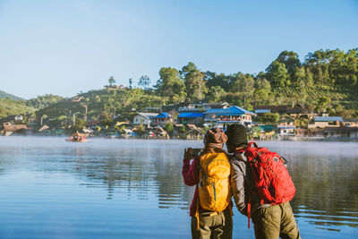 Rear view of people standing by lake against sky