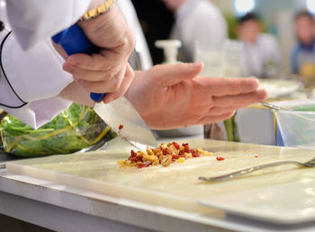 Cropped hands of chef chopping ingredients on cutting board in commercial kitchen