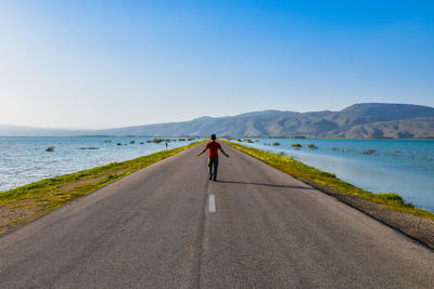 Rear view of man walking on road against sky