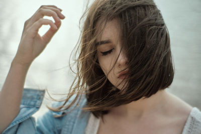 Close-up of young woman with tousled hair against lake