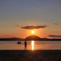 Silhouette people standing on beach against sky during sunset