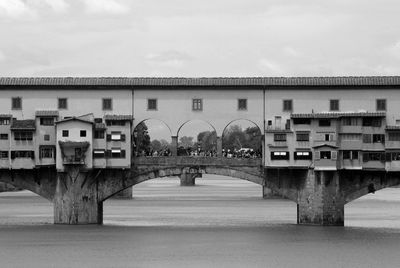 Arch bridge over river amidst buildings against sky