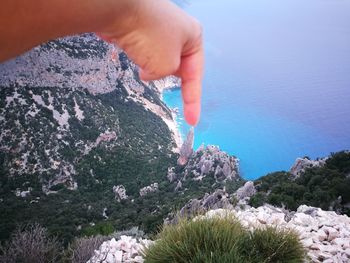 Cropped hand touching rock by sea