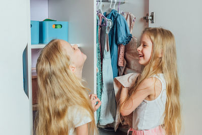 Two little beautiful girls friends sisters play fashion, choose outfits, clothes from a white