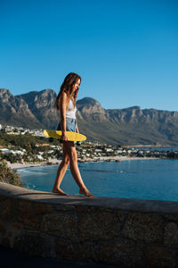 Side view of young woman against mountains against clear blue sky