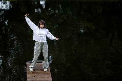 Rear view of young woman with arms outstretched standing in lake