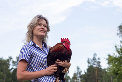 Side view of young woman holding rooster