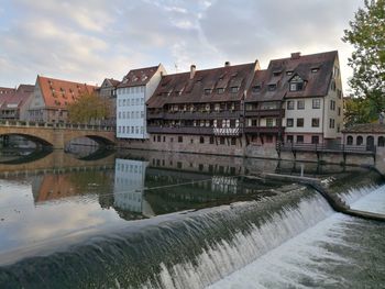 Buildings by river against sky