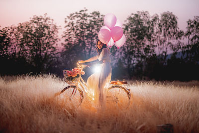 Woman holding balloons on field against sky at sunset