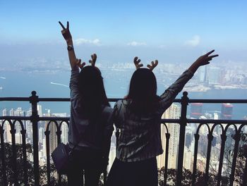 Rear view of friends gesturing peace sign while standing in balcony