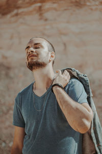 Young man with eyes closed holding denim jacket against wall