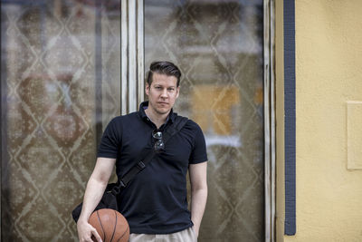 Close-up of mature man holding basketball while leaning against wall