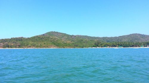 Scenic view of sea and mountains against clear blue sky