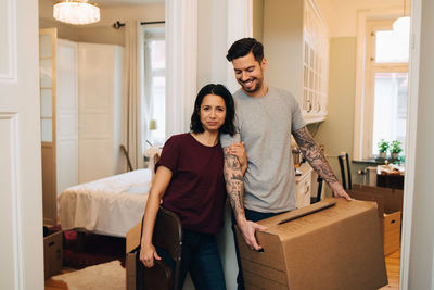 Portrait of woman standing with smiling man carrying box at home