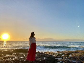 Woman standing on beach against sky during sunset