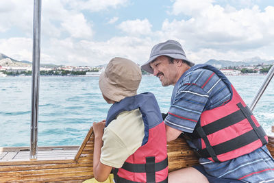 An asian boy in panama, life jacket and older man, his grandfather, trip on pleasure boat on sea.