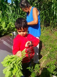 Boy by grandmother holding radishes at yard