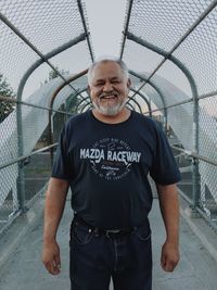 Portrait of smiling man standing by chainlink fence