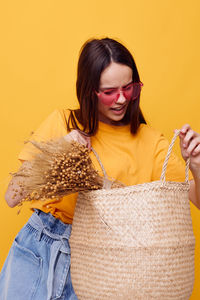 Teenage girl holding basket against yellow background