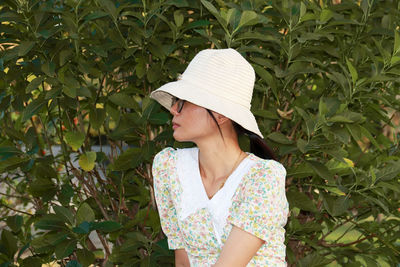 Midsection of woman wearing hat standing against plants