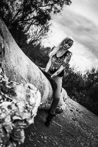 Portrait of young woman standing by tree against sky