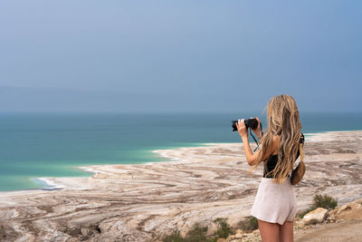 Rear view of woman standing by sea against clear sky