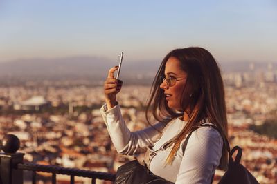 Young woman using mobile phone in city against sky